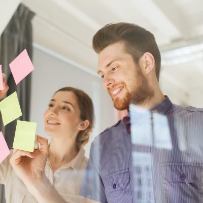 business, startup, planning, management and people concept - happy creative team writing on stickers at office glass board